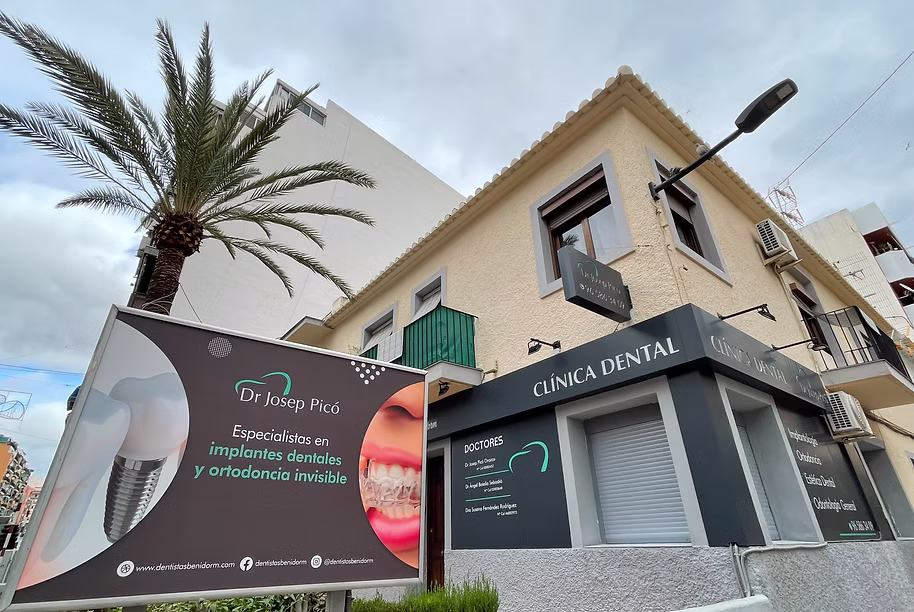 Außenansicht einer Zahnklinik in Benidorm, Spanien, mit Eingangsbereich und Werbeschildern für zahnärztliche Behandlungen.